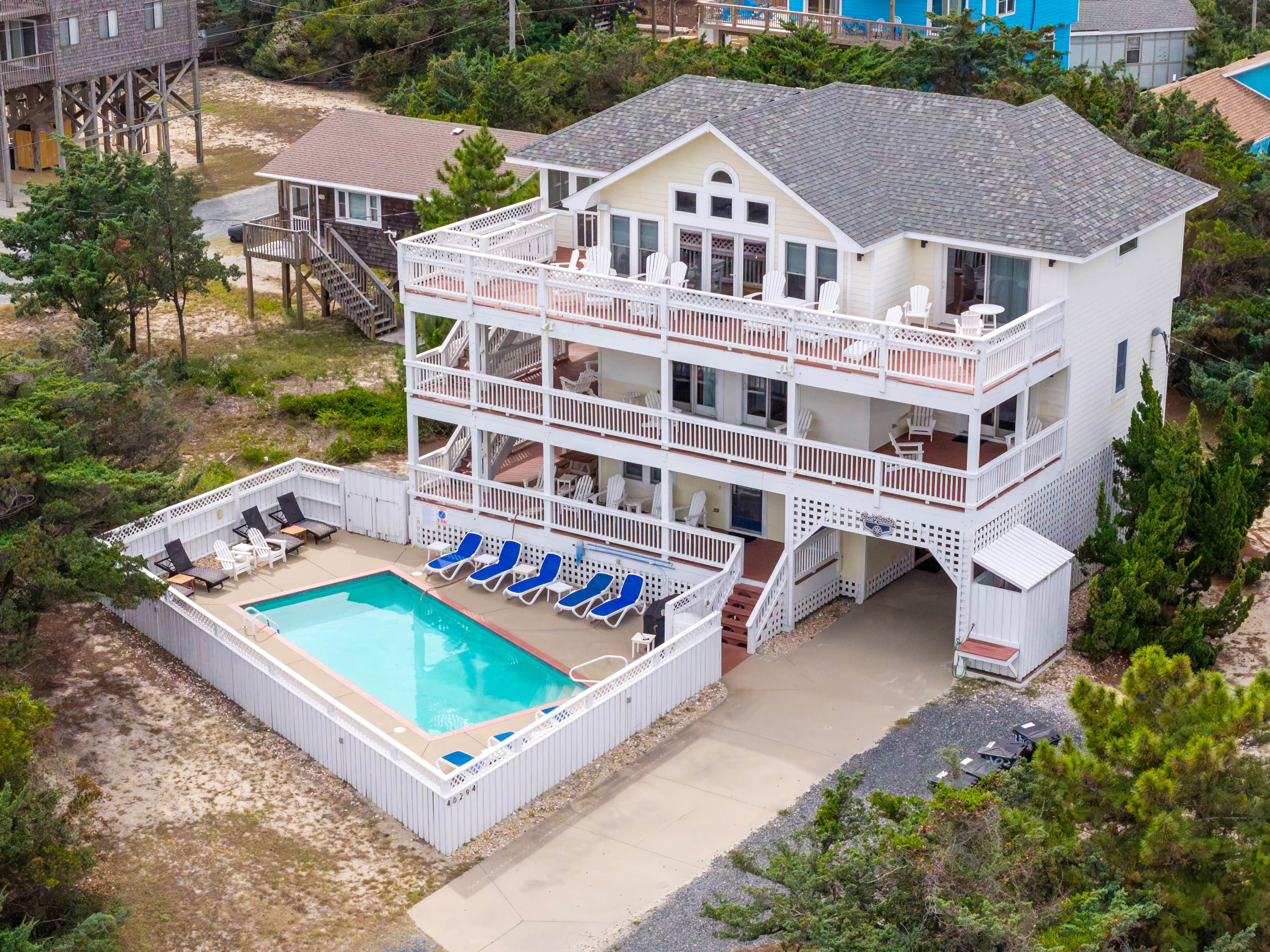 A multi-story beachfront property with a pool, outdoor seating, and a deck.