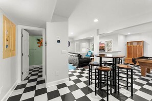 A room with a checkered floor, a pool table, a sofa, and a dining area with stools. - Good Latitude (Avon)