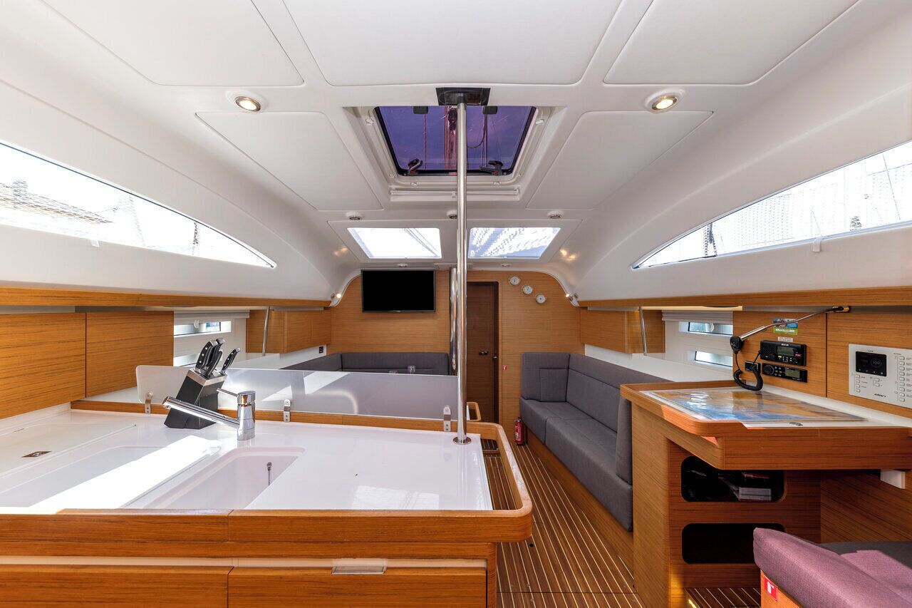 A boat interior with a central seating area, a small kitchen, and a control panel.