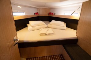 Eine kleine Kabine mit einem Einzelbett, einem Holz-Kopfteil und einem kleinen Fenster.