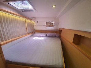 A single bed with a headboard, a skylight, and a window with curtains.