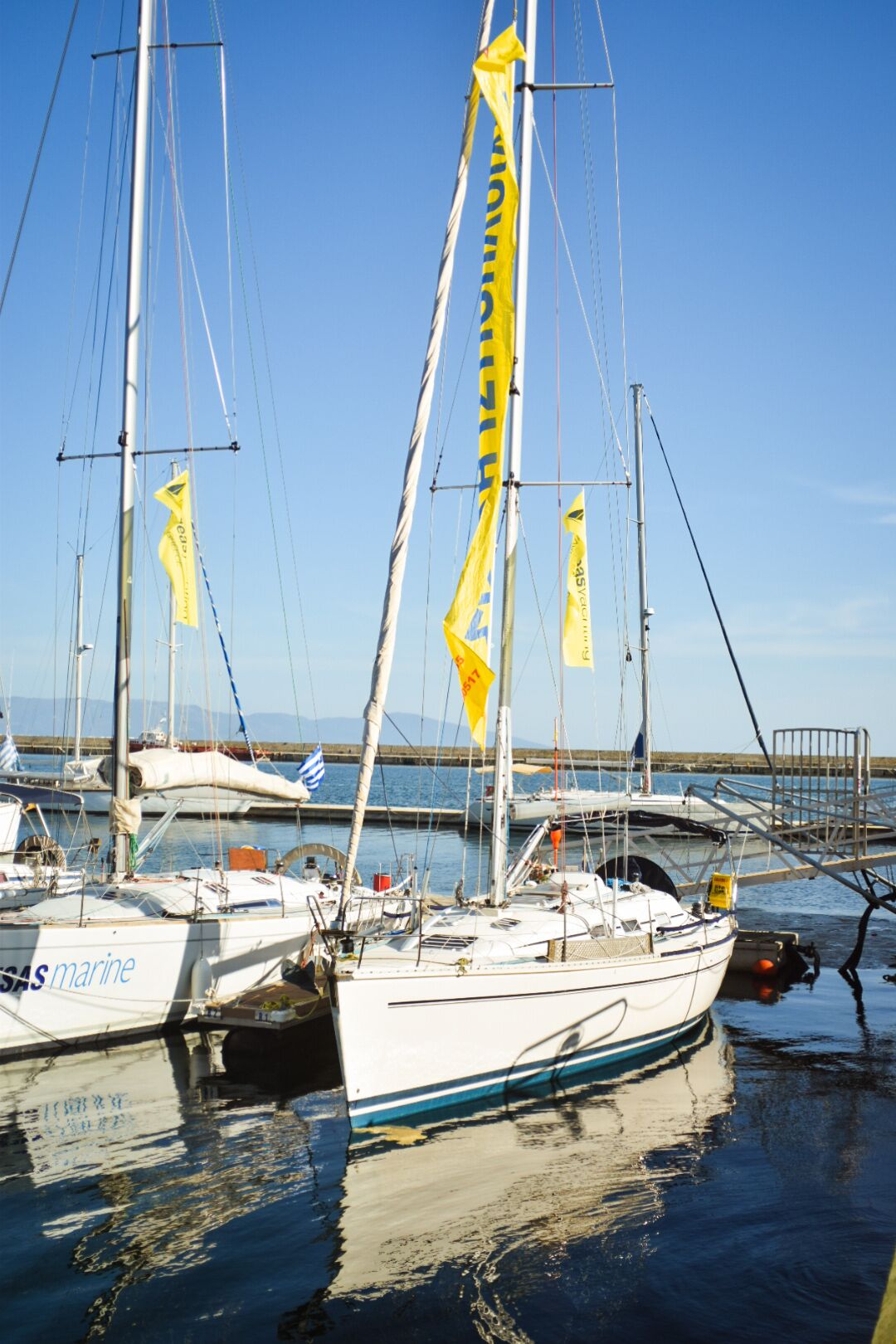 Un port de plaisance où sont amarrés de nombreux voiliers, dont certains arborent des drapeaux, avec un ciel dégagé en arrière-plan.