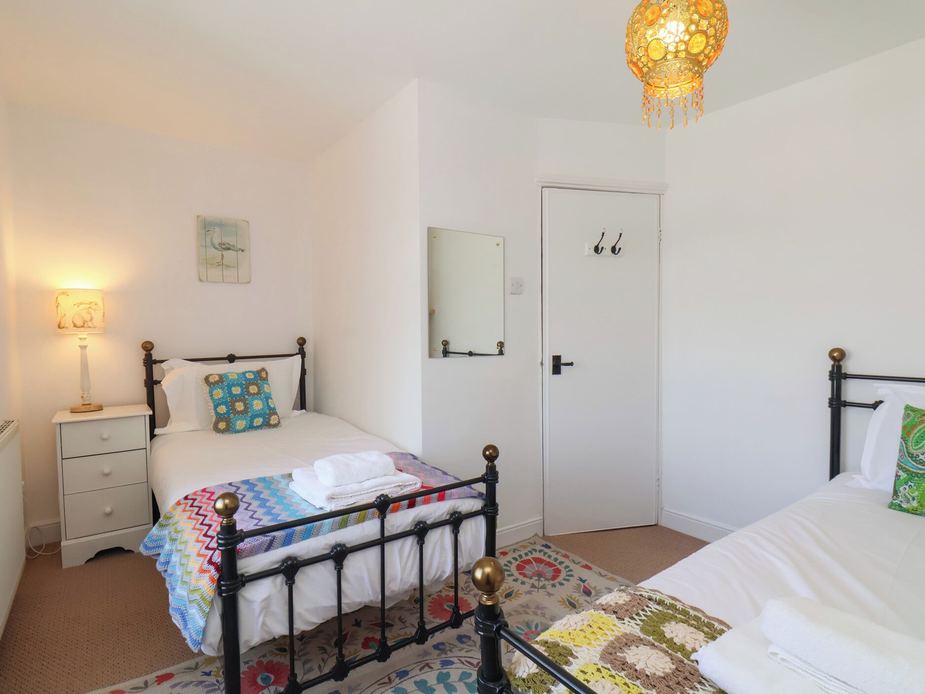 A bedroom with a bed, bedside table, lamp, mirror, door, and a hanging light fixture.