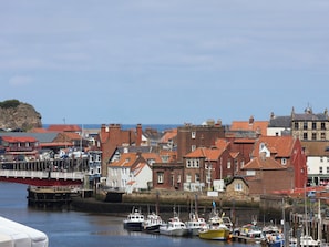A coastal town with historic buildings, a marina with boats, and a rocky outcrop in the distance.