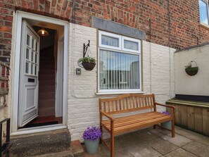 A wooden bench outside a building with a white door and window, a brick wall, and a hanging plant. - 4 Studley Terrace (Whitby)