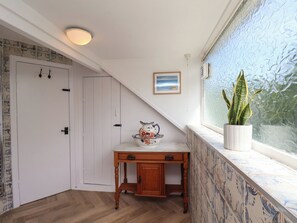 A room with a wooden floor, a white door, a small table with a decorative bowl, a potted plant, and a framed picture on the wall. - 4 Studley Terrace (Whitby)