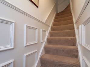 A staircase with a patterned carpet, white walls with decorative molding, and a wooden frame above the stairs.