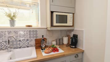 A kitchen with a sink, a microwave, and a window with blinds.
