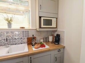 A kitchen with a sink, a microwave, and a window with blinds.