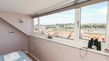 A bedroom with a large window, a bed, a pair of binoculars, and a small bottle on the windowsill.