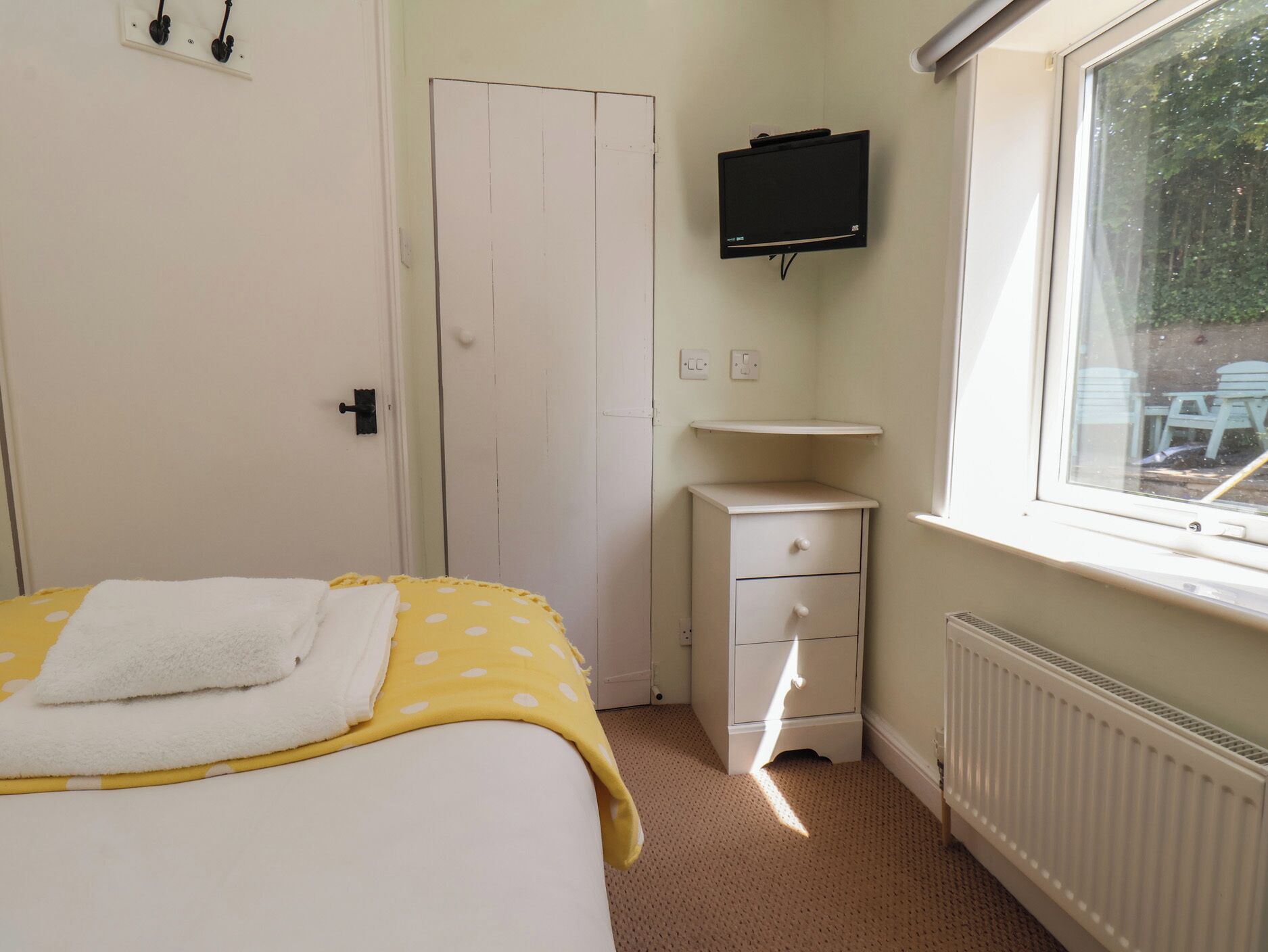 A bedroom with a bed, a bedside table, a TV on the wall, a window, and a radiator.
