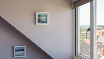 A room with a window, a painting on the wall, and a view of buildings outside.