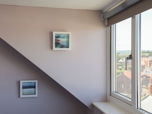 A room with a window, a painting on the wall, and a view of buildings outside.