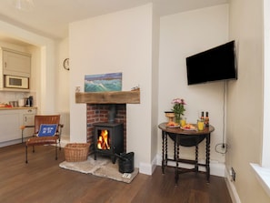 A living room with a fireplace, a television mounted on the wall, a dining table with breakfast items, and a kitchen in the background.