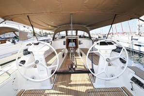 Ein Bootsdeck mit zwei Steuerhörnern, einer zentralen Bedieneinheit und Blick auf andere Boote im Hafen.
