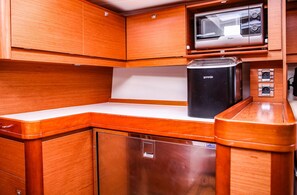 A compact kitchen with wooden cabinetry, a built-in microwave, a black refrigerator, and a sink. - Sun-Kissed Sailing Adventure in Sibenik, Croatia (Primošten)