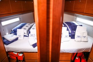 A cabin with two beds, each with a window, a white bedspread, and towels with a logo. - Sun-Kissed Sailing Adventure in Sibenik, Croatia (Primošten)