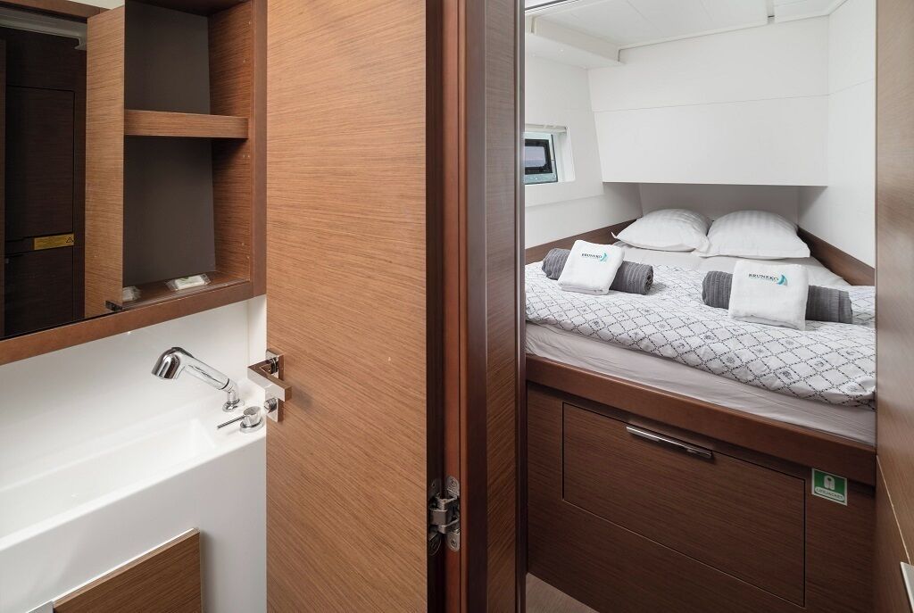 A compact room with a bed, a small bedside table, a built-in shelf, and a mirror.
