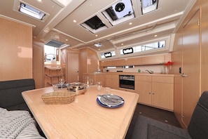 A compact kitchen with wooden cabinets, a dining table set for four, and a small window above the sink. - Sun-Kissed Sailing Adventure in Zadar, Croatia (Biograd na moru)