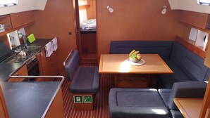 A compact kitchen with a stove, sink, and a small table with a fruit bowl. There is a bench and a cushioned seating area. - Sun-Kissed Sailing Adventure in Islas Baleares, Mallorca (Palma)