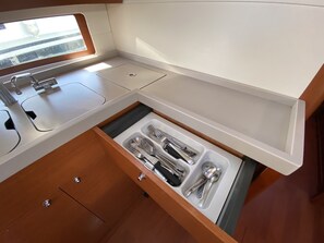 A compact kitchen with a built-in sink, a drawer with utensils, and a window for natural light. - Sun-Kissed Sailing Adventure in the Majestic Islas Baleares (Ibiza / Eivissa)