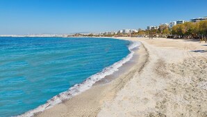 A beach with clear blue water, a sandy shore, and buildings in the background. - Sun-Kissed Sailing Adventure in Islas Sarónicas (Alimos)