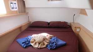 A compact bed with a dark-colored mattress, two pillows, and a neatly folded towel arrangement on the bed. - Sun-Kissed Sailing Adventure in Phuket (Mai Khao)