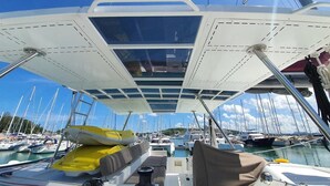 A boat deck with a covered seating area, a small table, and a yellow life preserver. - Sun-Kissed Sailing Adventure in Phuket (Mai Khao)