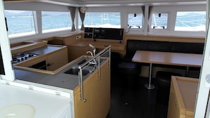 A compact galley with a stove, sink, and a small dining area with a table and bench. - Sun-Kissed Sailing Adventure in Phuket (Mai Khao)