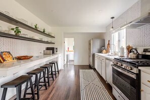 A modern kitchen with a herringbone-patterned backsplash, wooden flooring, and a central island with bar stools. - The Fireside: A Catskills Escape with Wide Open Spaces (Prattsville)
