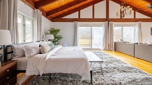 Ein Schlafzimmer mit Bett, Nachttisch, Lampe, Vorhängen, Fenstern und Deckenventilator.