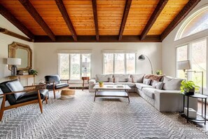 A spacious living room with a high wooden ceiling, a large sofa, a coffee table, and a patterned rug. - The Fireside: A Catskills Escape with Wide Open Spaces (Prattsville)
