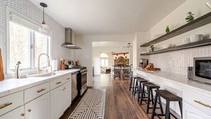 Eine moderne Küche mit weißen Schränken, einer zentralen Kochinsel, Barhocker und einer Rückwand mit Fischgrätmuster.