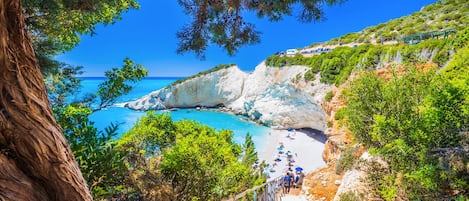 A coastal path leading to a beach with a rocky cliff and a clear blue sea.