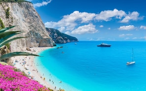 A coastal beach with clear turquoise waters, a rocky cliff, and a sailboat. - Sun-Kissed Sailing Adventure in the Ionian Islands, Lefkada (Lefkada)