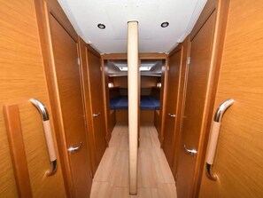 A narrow corridor with wooden walls and a central column, leading to a bunk area with blue bedding.