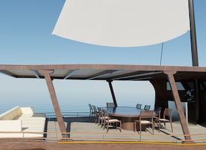 A covered outdoor dining area with a table and chairs, overlooking a body of water.