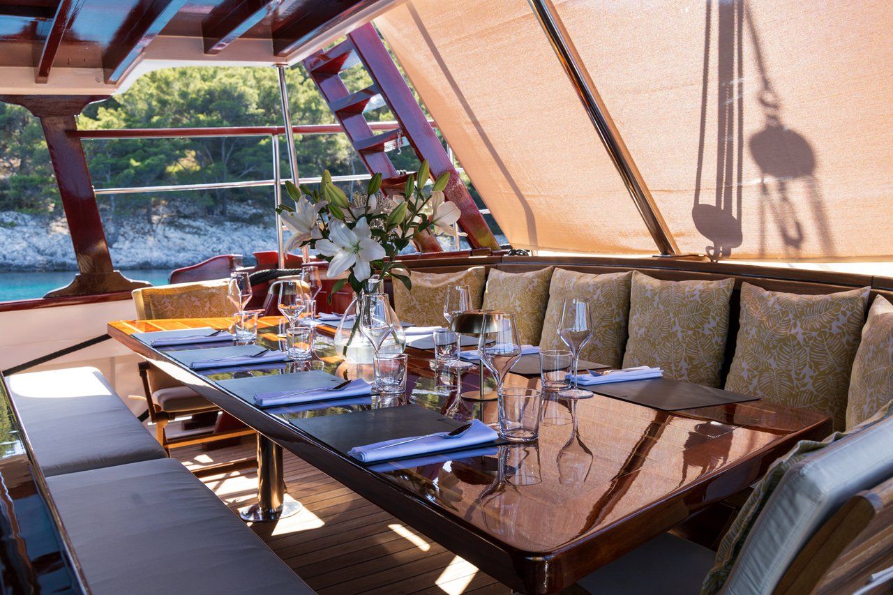 A dining table set with glasses, plates, and cutlery, surrounded by cushioned seating.