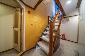 A staircase with a wooden handrail, carpeted steps, a fire extinguisher, and a door with a glass panel.