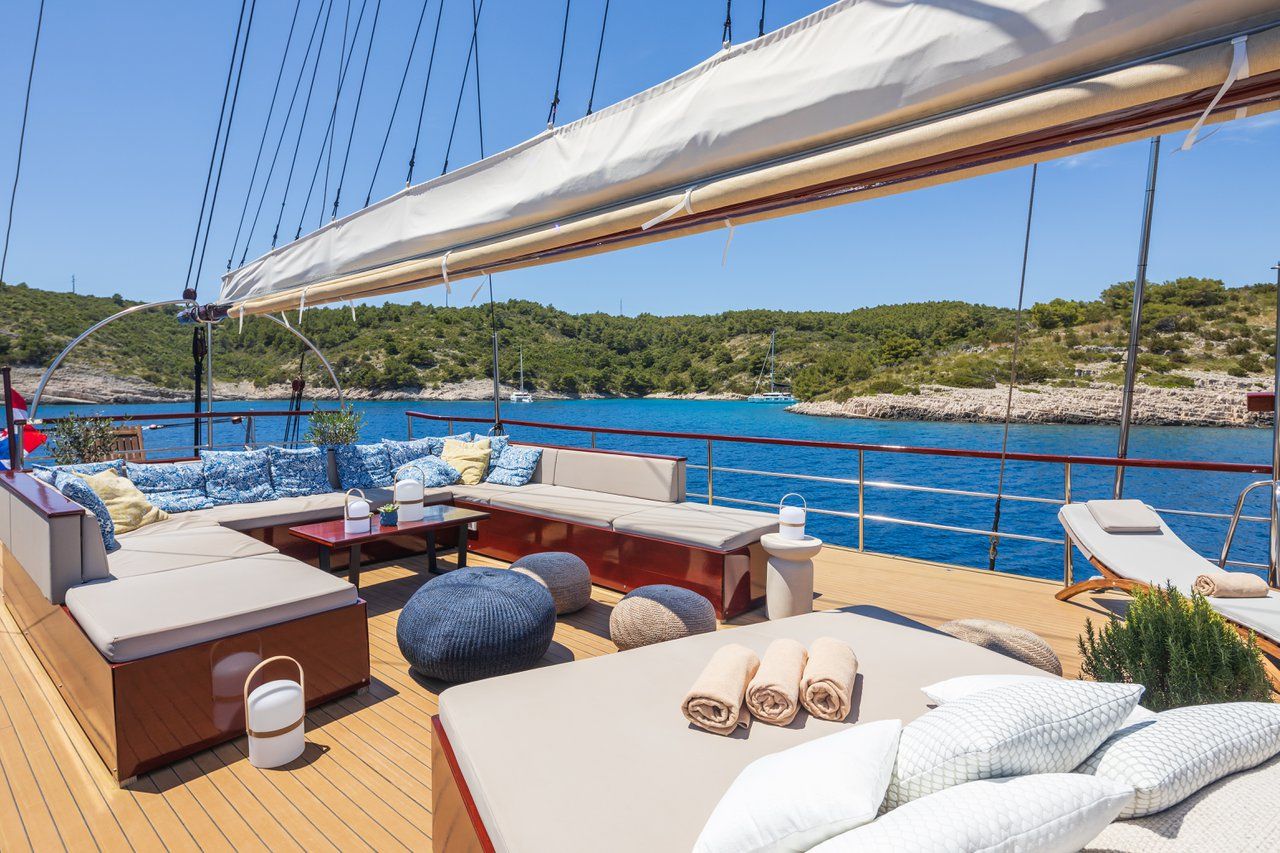 A yacht deck with a sofa, ottoman, and lounge chairs, a table, and a canopy.