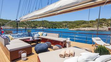 A yacht deck with a sofa, ottoman, and lounge chairs, a table, and a canopy.