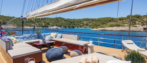 A yacht deck with a sofa, ottoman, and lounge chairs, a table, and a canopy.