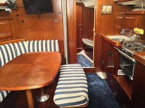 A compact galley with a wooden table, striped bench, and a small kitchenette. - Sun-Kissed Sailing Adventure in the Ionian Islands, Lefkada (Lefkada)