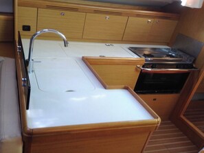 A compact kitchen with a sink, stove, and wooden cabinets. - Sun-kissed Sailing Adventure in the Ionian Islands (Preveza)