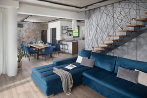 A modern living space with a blue sofa, dining area, kitchen, and staircase. - 5BR Modern Villa & Heated Pool & Ensuite Baths (Brgod)