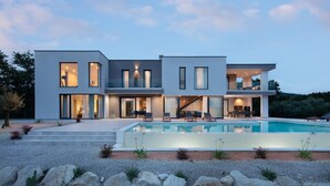 Ein modernes, zweistöckiges Haus mit Schwimmbad, großen Fenstern und einem hellen Innenraum.