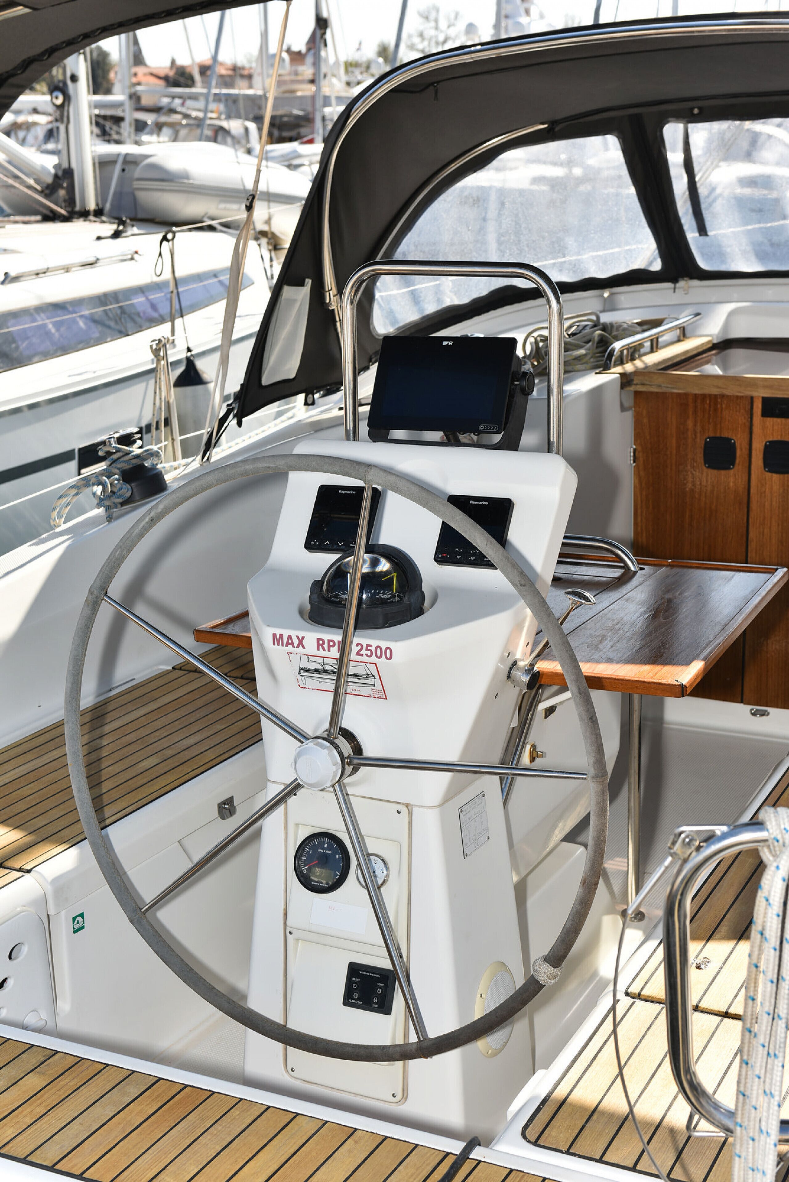 A boat's helm station with a steering wheel, control panel, and wooden deck.