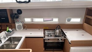 A compact galley kitchen with a sink, stove, and oven, wooden cabinetry, and a window above the stove.