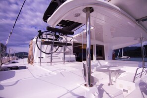 Le pont d’un yacht, doté d’un espace salon abrité, d’un mât et offrant une vue sur la mer.
