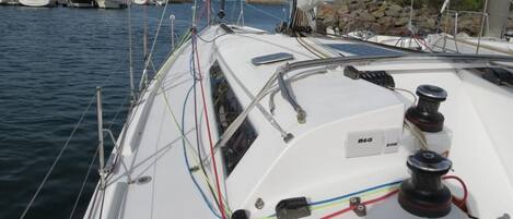 Le pont d’un voilier, avec un panneau de commande B&G, divers cordages et, en arrière-plan, une côte rocheuse.
